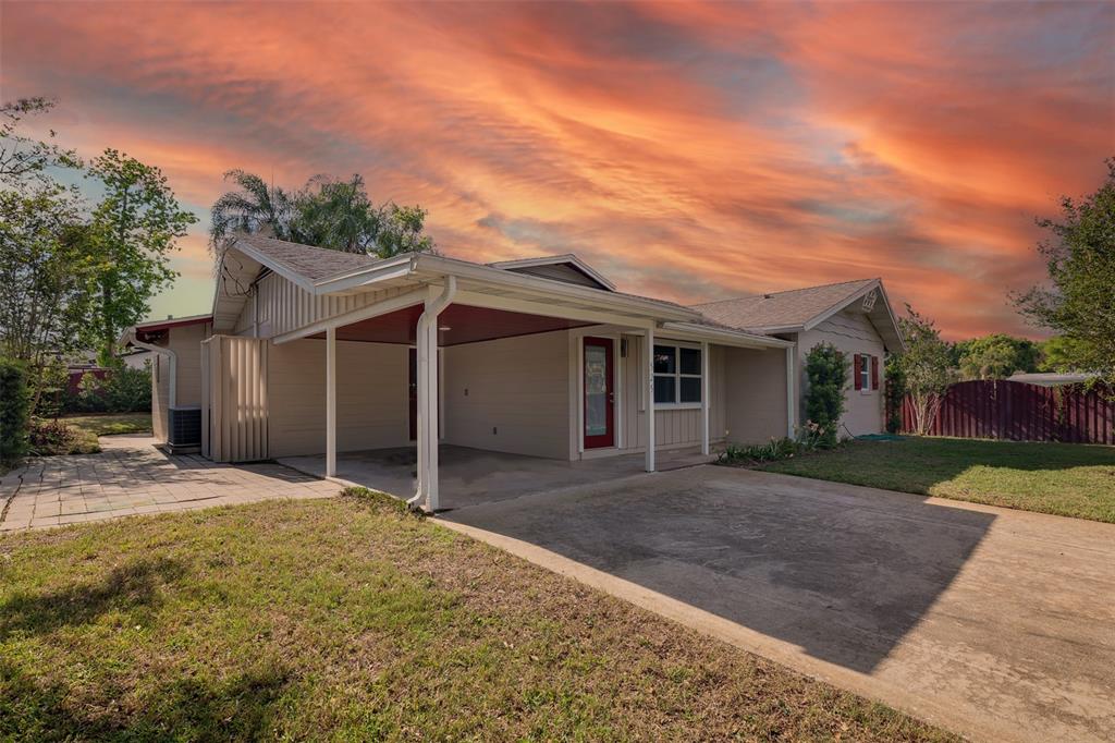 A single-story house exterior features a concrete driveway, a covered carport, and a red door — 525 OLOLU DRIVE, WINTER PARK, FL