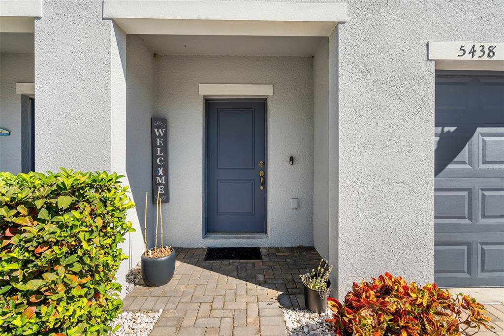 A gray front door with a welcome sign sits under a covered entryway with pavers — 5438 TRIPOLI DRIVE, PALMETTO, FL