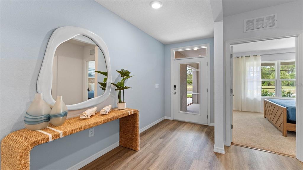 An entryway features a woven console table, a large organic-shaped mirror, and light wood flooring — 1332 FOUNTAIN VIEW STREET, ORMOND BEACH, FL