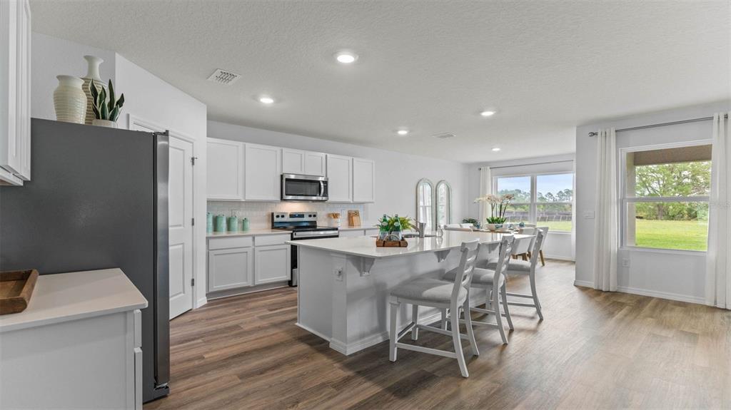 A modern kitchen features white cabinets, a large island with seating, and wood-look flooring — 1332 FOUNTAIN VIEW STREET, ORMOND BEACH, FL