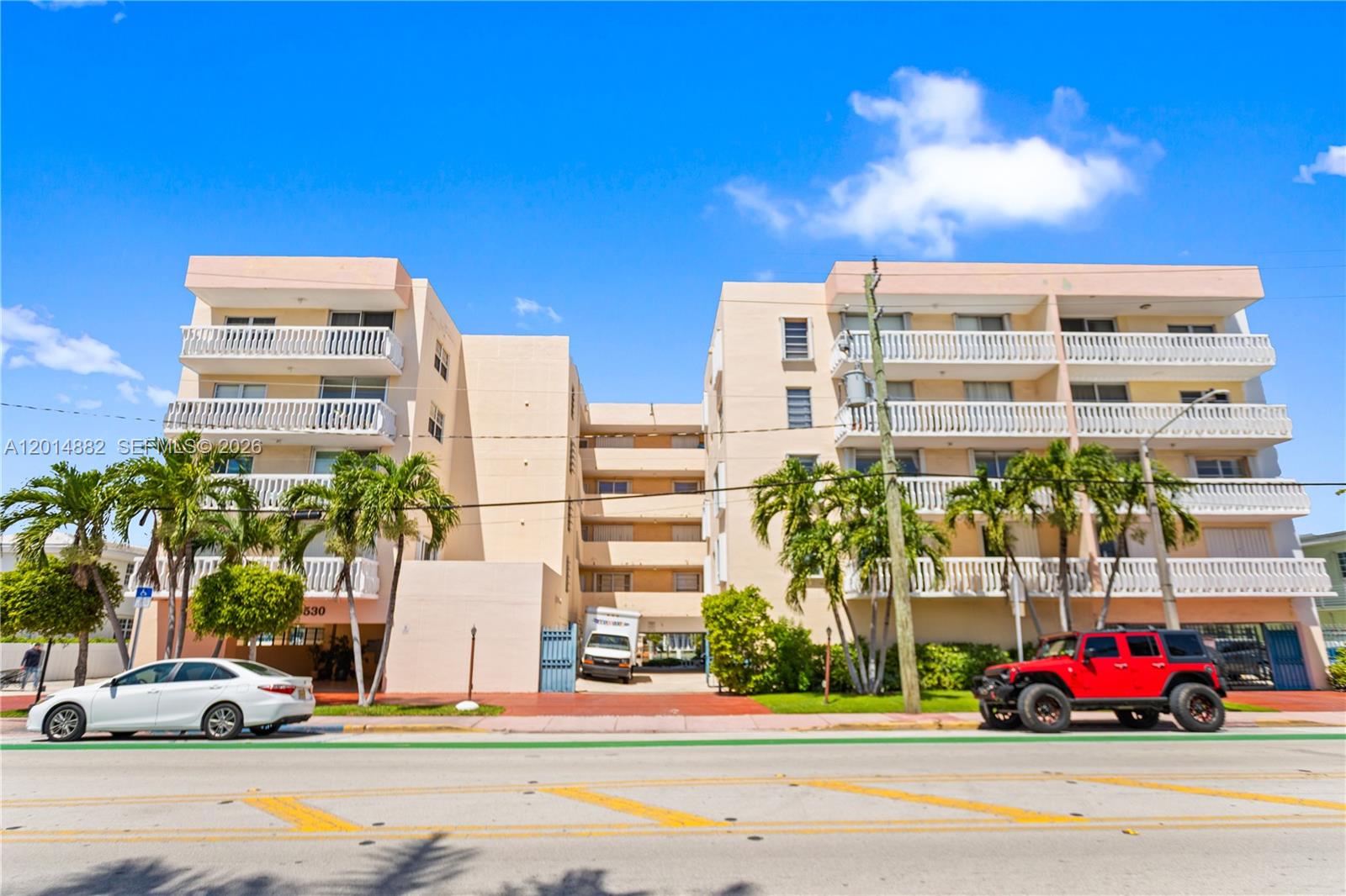 A multi-story apartment building with balconies and palm trees sits behind a street — 8530 Byron Ave # 302, Miami Beach FL 33141, MIAMI BEACH, FL
