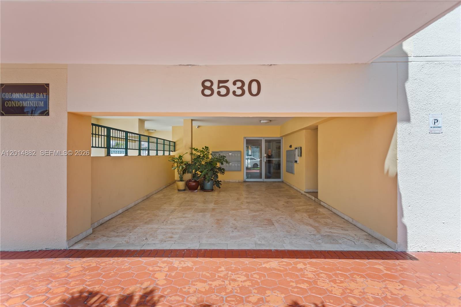 The entrance to a condominium building features a covered walkway with tiled flooring and plants — 8530 Byron Ave # 302, Miami Beach FL 33141, MIAMI BEACH, FL