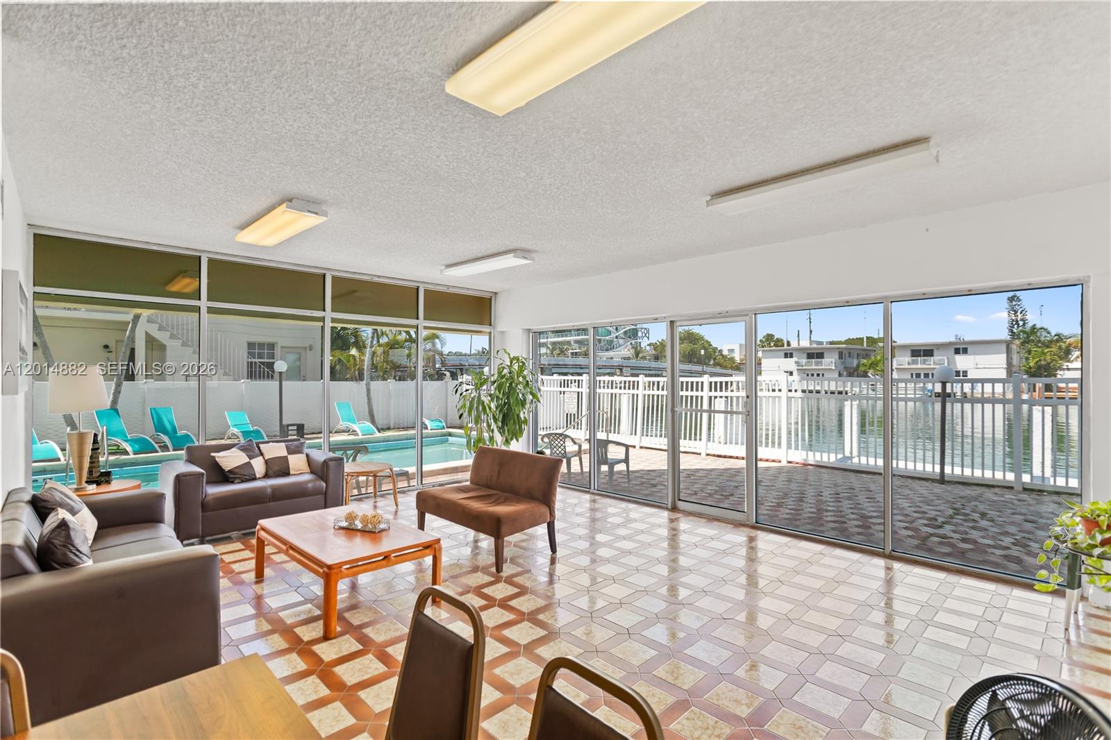 A sunroom with tile flooring, large glass walls, and views of a pool and canal — 8530 Byron Ave # 302, Miami Beach FL 33141, MIAMI BEACH, FL