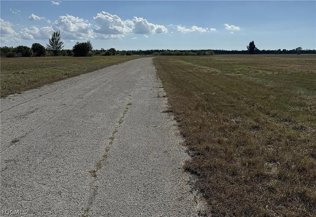 A paved road stretches through a large, flat, grassy field under a blue sky — 14033 TORPEDO-RAY PLACE, PLACIDA, FL