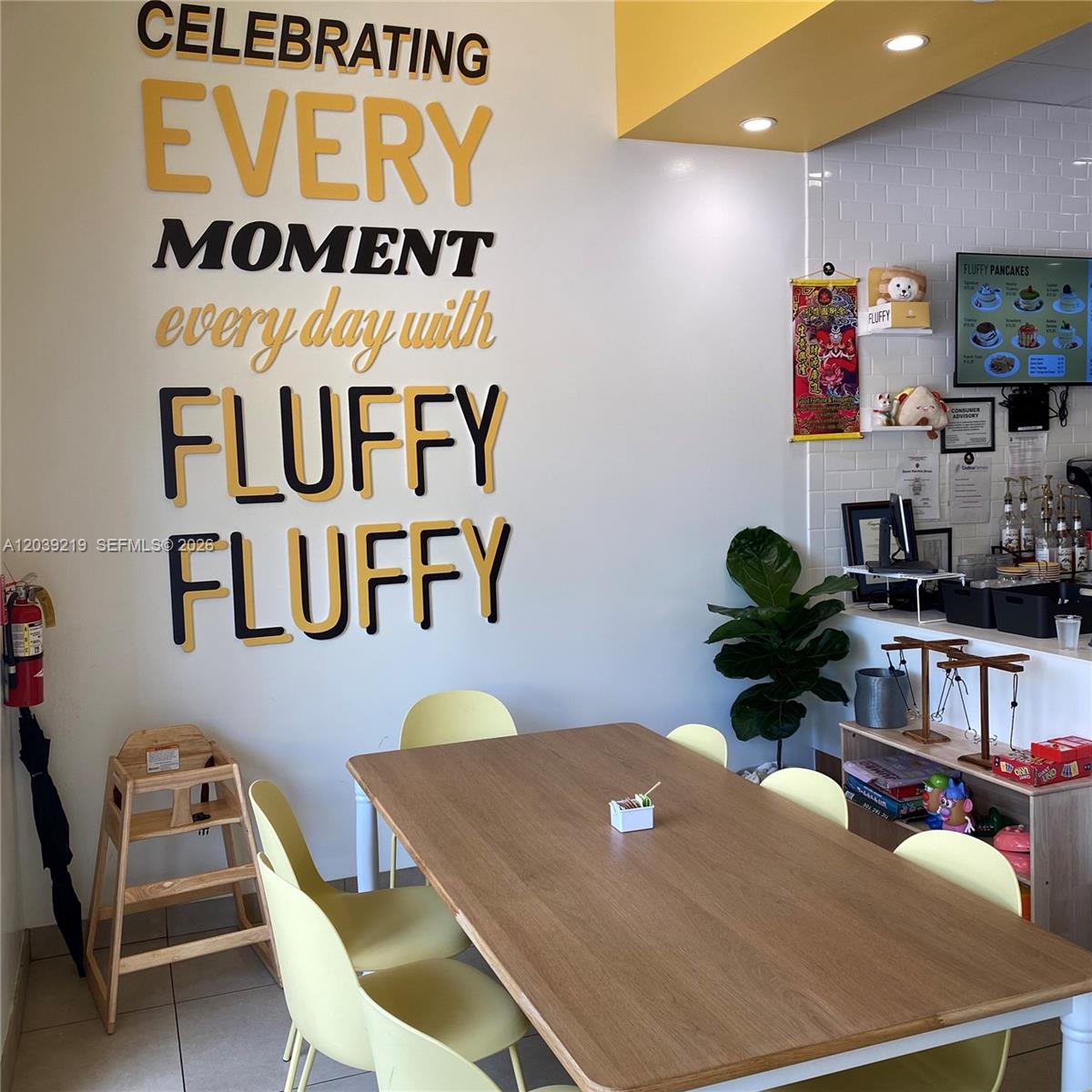 A dining area features a wooden table, yellow chairs, and wall lettering in a cafe — 5241 NW 87th Ave D104, Doral FL 33178, DORAL, FL