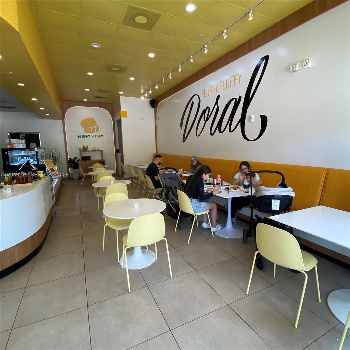 A bright cafe interior features yellow seating, white tables, and a large wall mural — 5241 NW 87th Ave D104, Doral FL 33178, DORAL, FL
