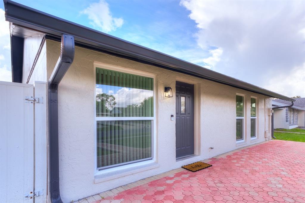 A view of a house exterior featuring a gray front door, large windows, and red pavers — 8541 BRIAR GROVE CIRCLE, TAMPA, FL