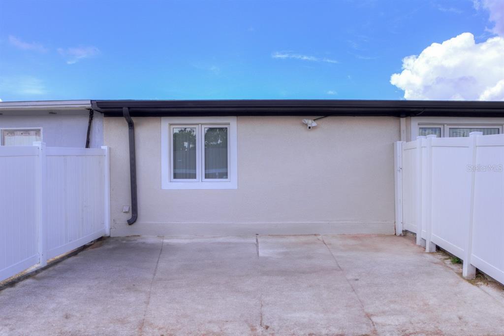 A concrete patio sits between two white vinyl privacy fences against a stucco house wall — 8541 BRIAR GROVE CIRCLE, TAMPA, FL