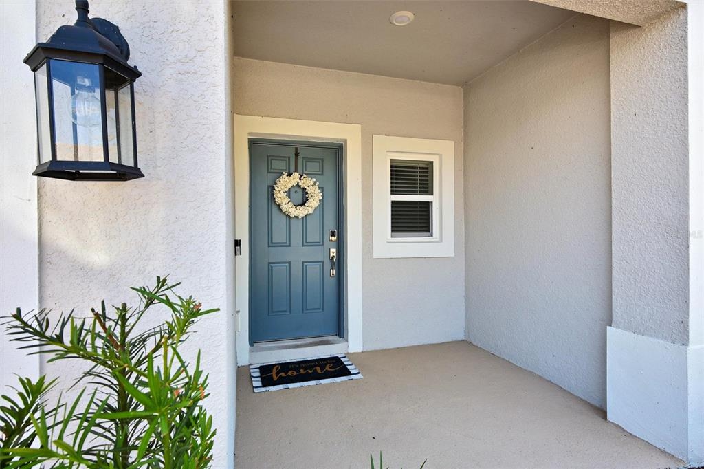 A blue front door with a wreath sits under a covered porch with a light — 1414 ANCHOR BEND WAY, KISSIMMEE, FL