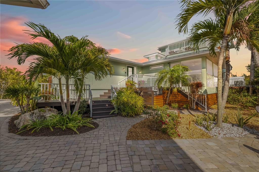 A two-story house with a wooden deck, palm trees, and a paved patio at sunset — 7885 MANASOTA KEY ROAD, ENGLEWOOD, FL