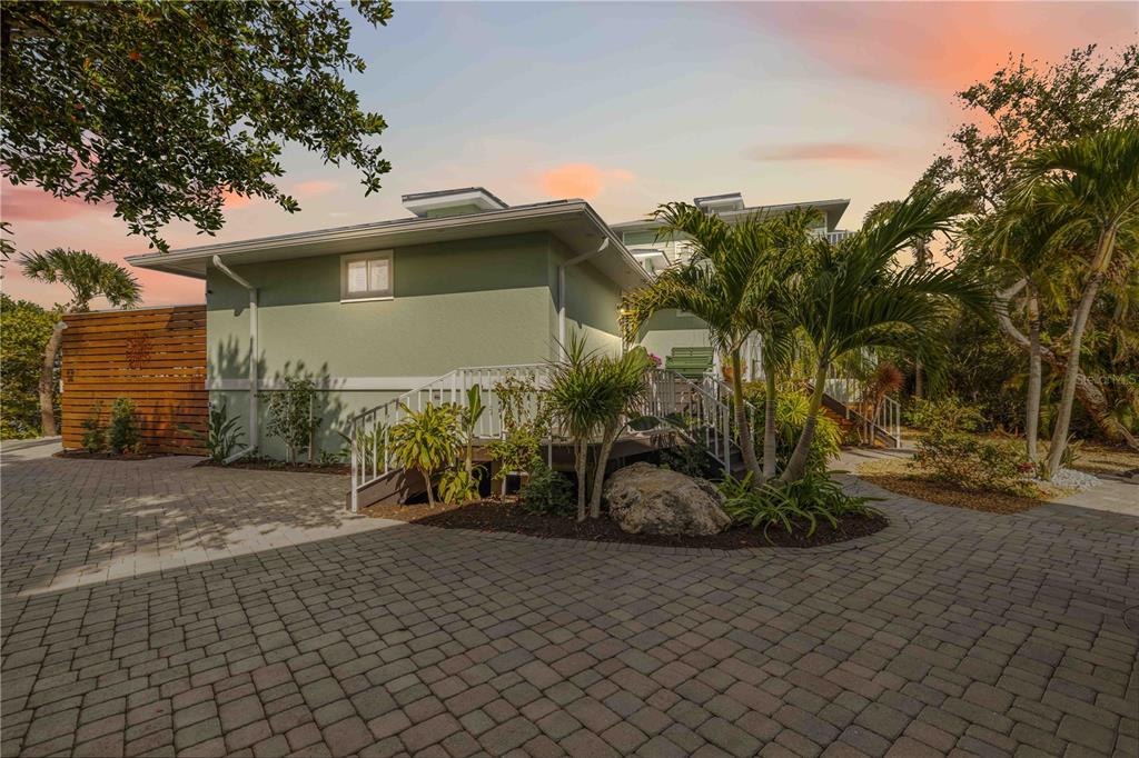 A light green house with a paved driveway, wooden privacy fence, and tropical landscaping — 7885 MANASOTA KEY ROAD, ENGLEWOOD, FL