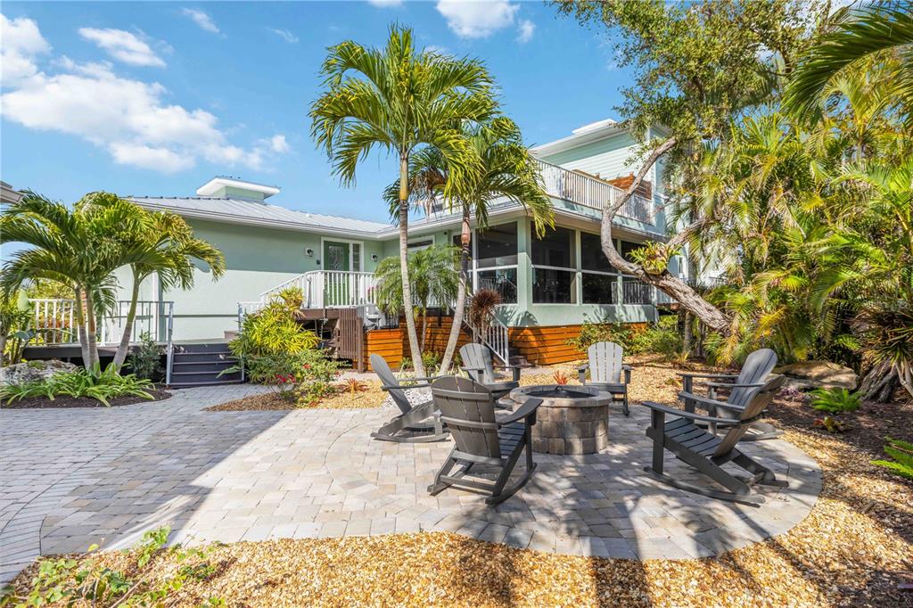 A stone patio with a fire pit and rocking chairs sits outside a light green house — 7885 MANASOTA KEY ROAD, ENGLEWOOD, FL