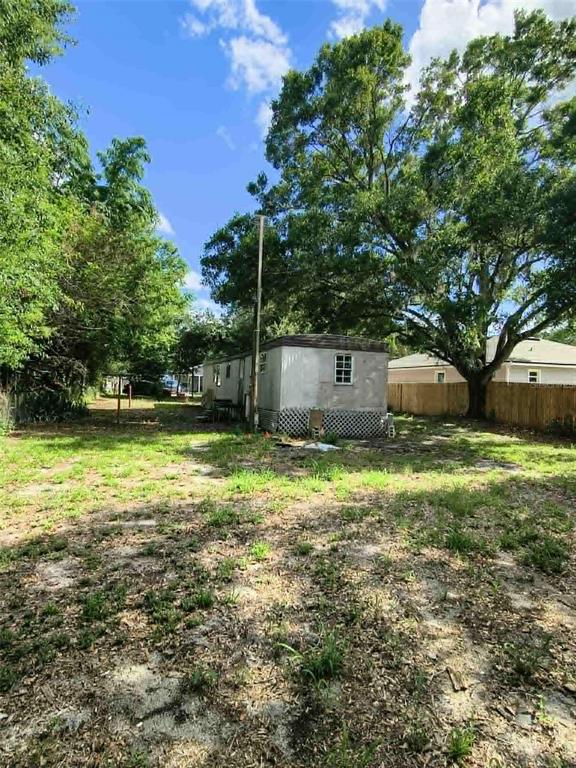 A mobile home sits in a grassy, tree-shaded yard with a wooden fence — 2840 EATON AVENUE, LAKELAND, FL