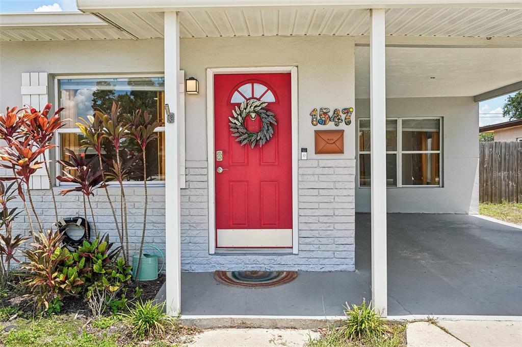 The exterior of a house features a bright red front door, a carport, and landscaping — 1547 56TH AVENUE N, ST PETERSBURG, FL