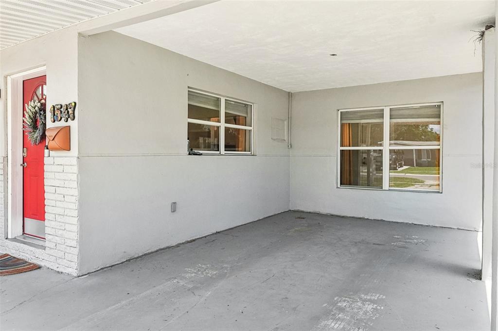 A covered concrete carport area features a red front door and two windows — 1547 56TH AVENUE N, ST PETERSBURG, FL