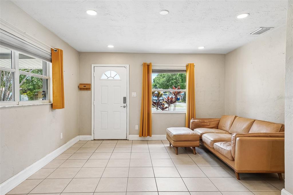 A living room with beige tile floors, a tan leather sofa, and a white front door — 1547 56TH AVENUE N, ST PETERSBURG, FL
