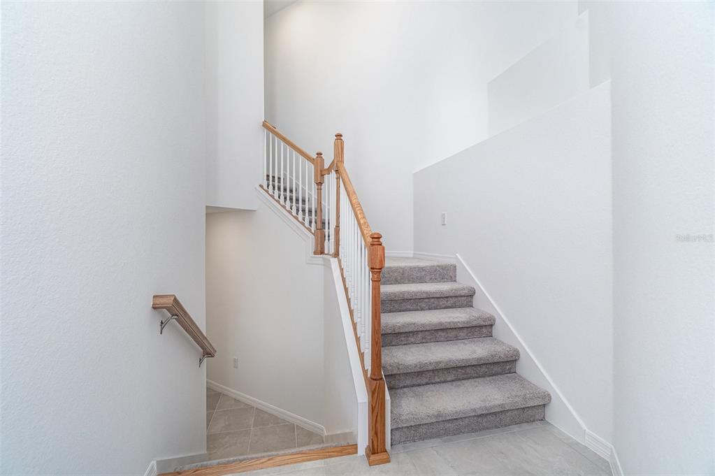 A staircase with carpeted steps and a wooden railing leads to an upper level — 15194 BLUFFTON LANE UNIT 1421, PUNTA GORDA, FL