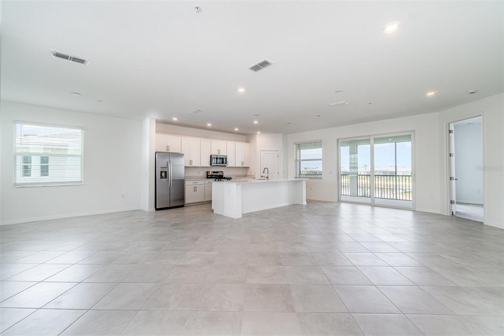 A spacious, open-concept kitchen and living area with white cabinetry, tile flooring, and sliding doors — 15194 BLUFFTON LANE UNIT 1421, PUNTA GORDA, FL