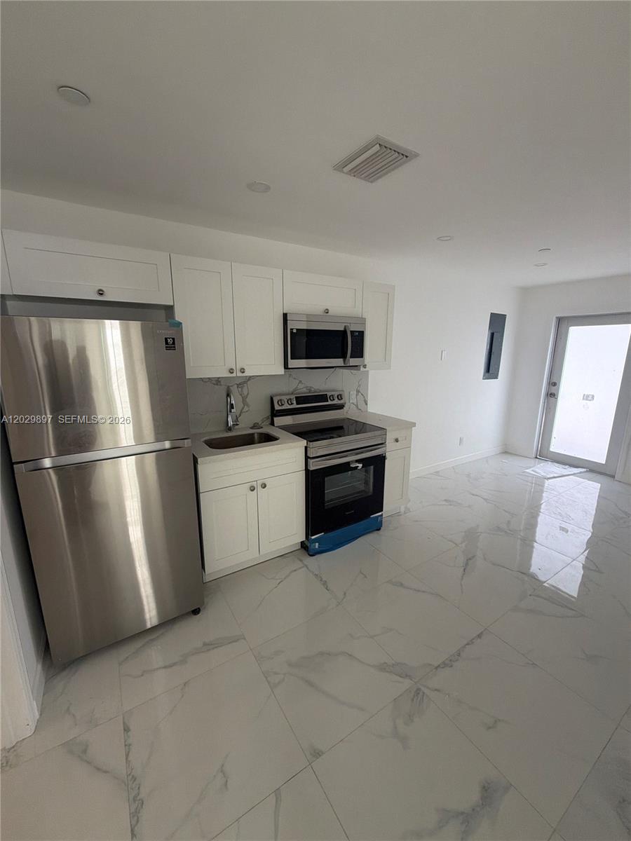 A modern kitchen features white cabinets, stainless steel appliances, and white marble-patterned tile flooring — 729 SW 3rd St # 2, Miami FL 33130, MIAMI, FL