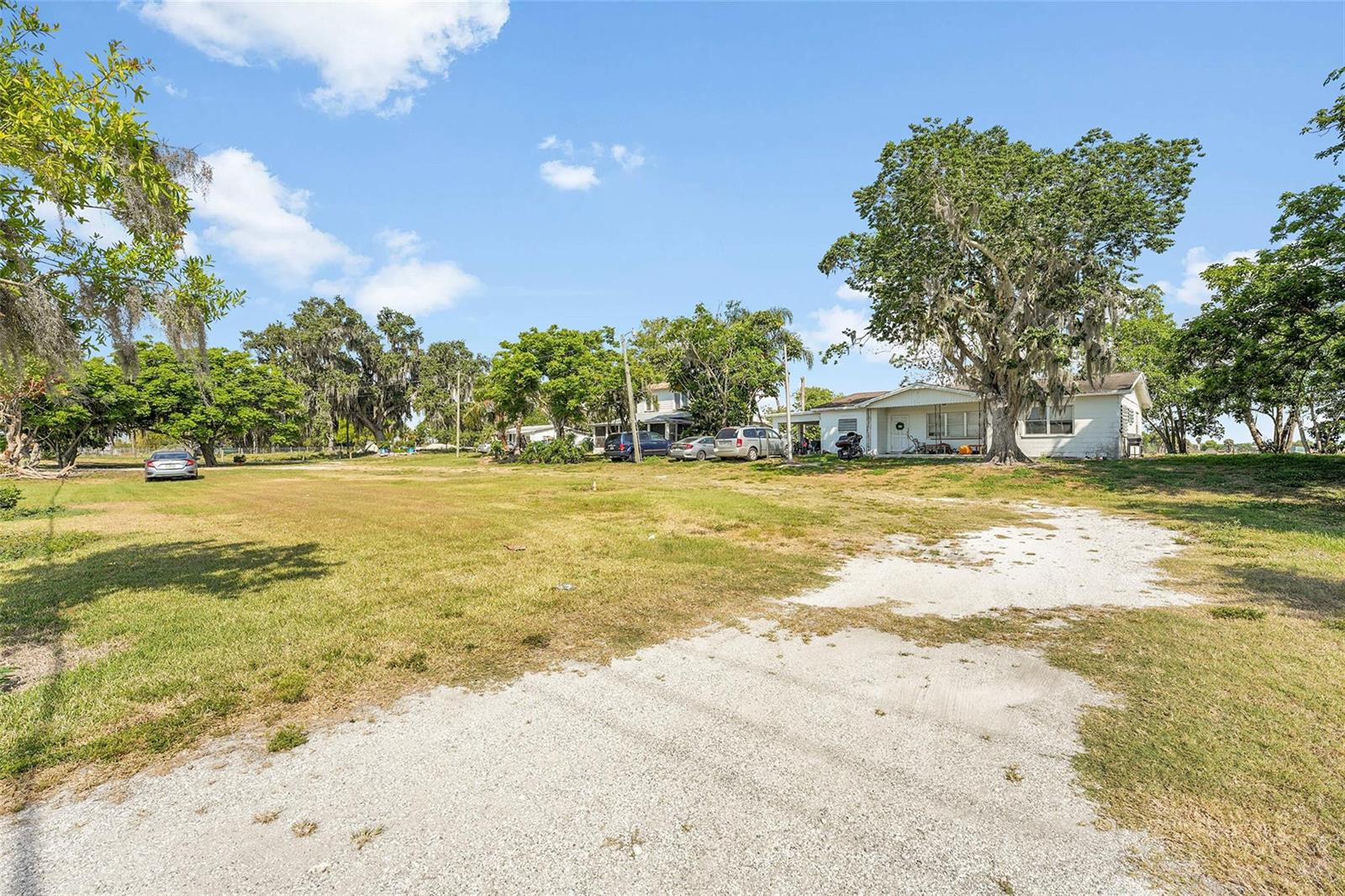 A large grassy yard leads to a white house shaded by several mature oak trees — 672 State Road 78, Okeechobee FL 34974, OKEECHOBEE, FL