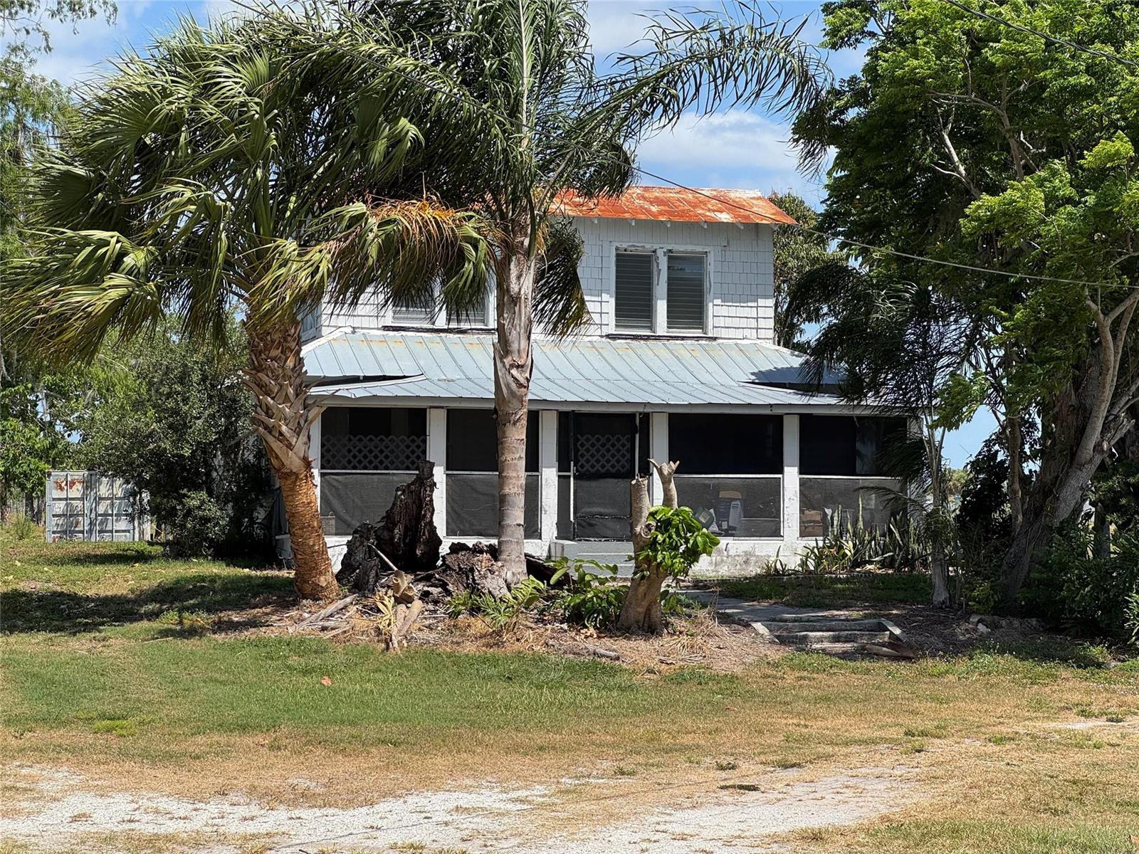 A two-story house with a screened porch and a rusted metal roof sits outdoors — 672 State Road 78, Okeechobee FL 34974, OKEECHOBEE, FL