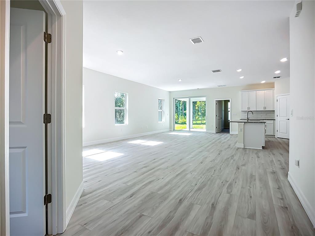 An open-concept living area features light wood-look flooring, white walls, and a kitchen with island — 1529 GERANIUM AVENUE, NORTH PORT, FL