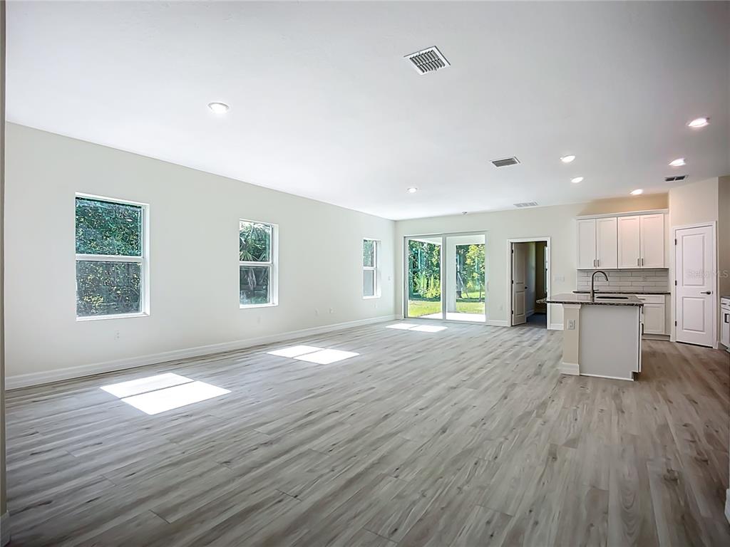 A spacious, open-concept living area features light wood-look flooring, white walls, and a modern kitchen — 1529 GERANIUM AVENUE, NORTH PORT, FL