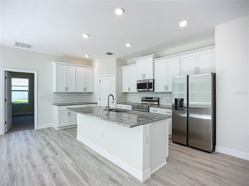A modern kitchen features white cabinets, granite countertops, a central island, and stainless steel appliances — 1529 GERANIUM AVENUE, NORTH PORT, FL