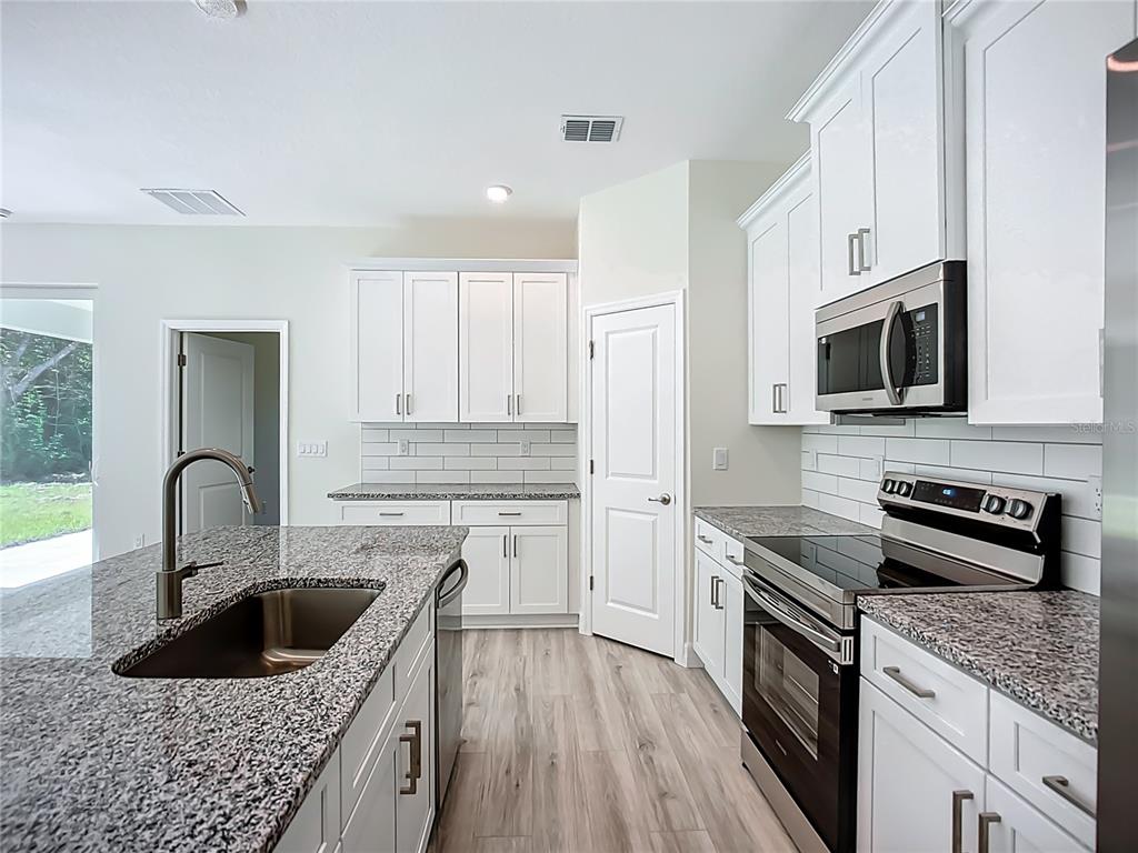 A modern kitchen features white cabinets, granite countertops, stainless steel appliances, and wood-look flooring — 1529 GERANIUM AVENUE, NORTH PORT, FL