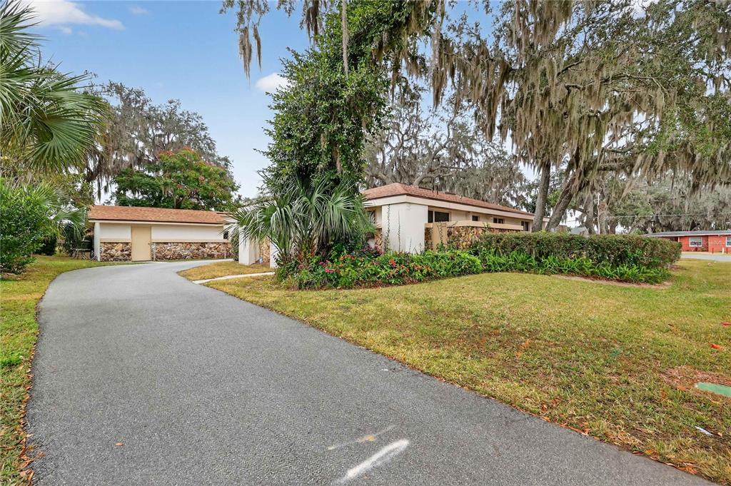 A paved driveway leads to a single-story house with stone accents and mature oak trees — 708 LEE STREET, LEESBURG, FL