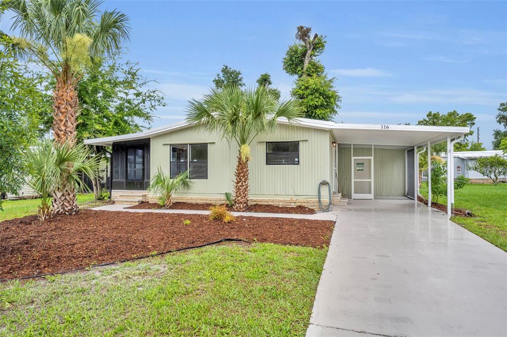 A light green single-story house features a concrete driveway, a carport, and palm trees — 116 CYPRESS ROAD, WILDWOOD, FL