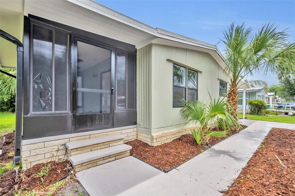 A light green mobile home exterior features a screened-in porch, concrete steps, and landscaping — 116 CYPRESS ROAD, WILDWOOD, FL