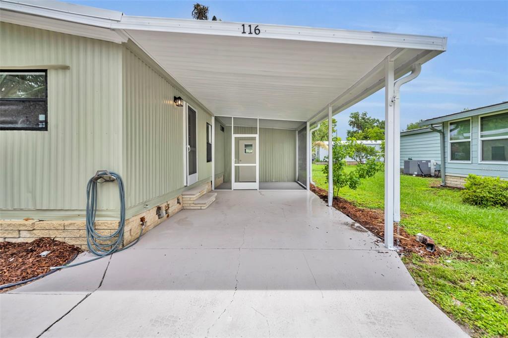 A covered concrete carport leads to a screened-in porch entrance of a light green home — 116 CYPRESS ROAD, WILDWOOD, FL