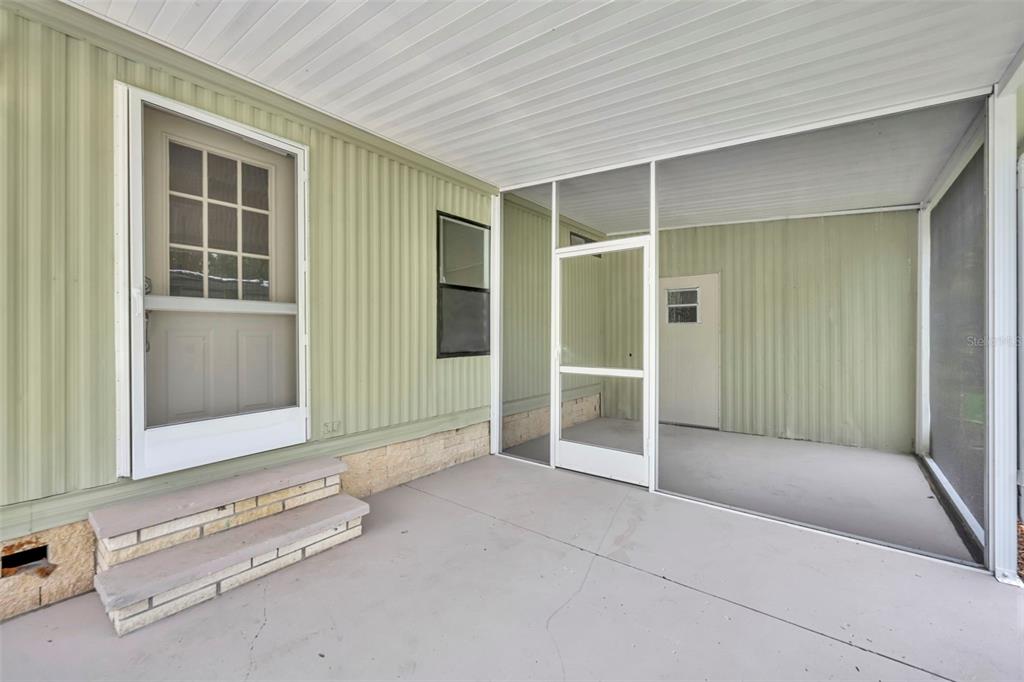 A covered patio with a screened-in area, light green siding, and concrete steps — 116 CYPRESS ROAD, WILDWOOD, FL
