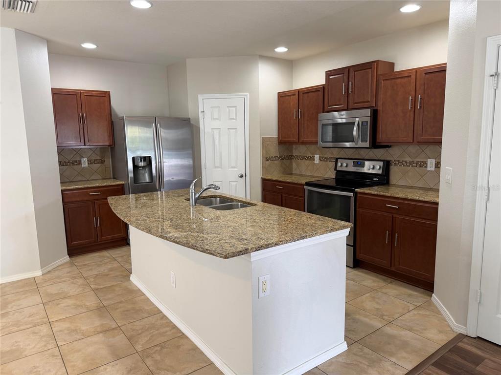 A kitchen features dark wood cabinets, granite countertops, stainless steel appliances, and a central island — 4723 SOMERSET HILL LANE, RIVERVIEW, FL
