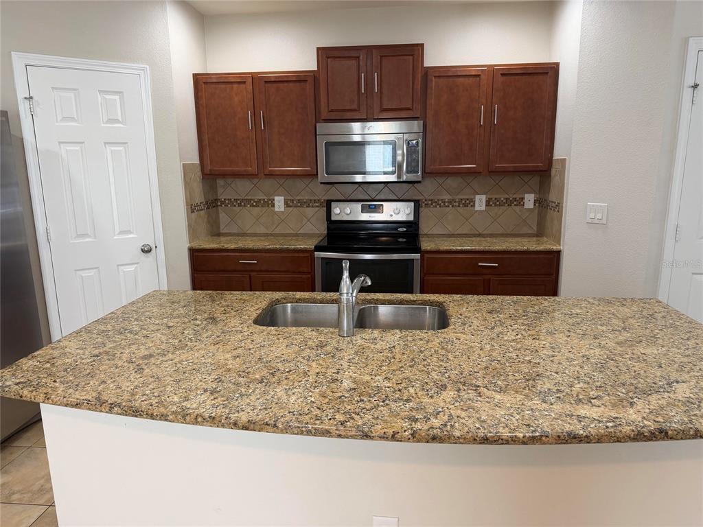 A kitchen features dark wood cabinets, granite countertops, a stainless steel stove, and an island — 4723 SOMERSET HILL LANE, RIVERVIEW, FL