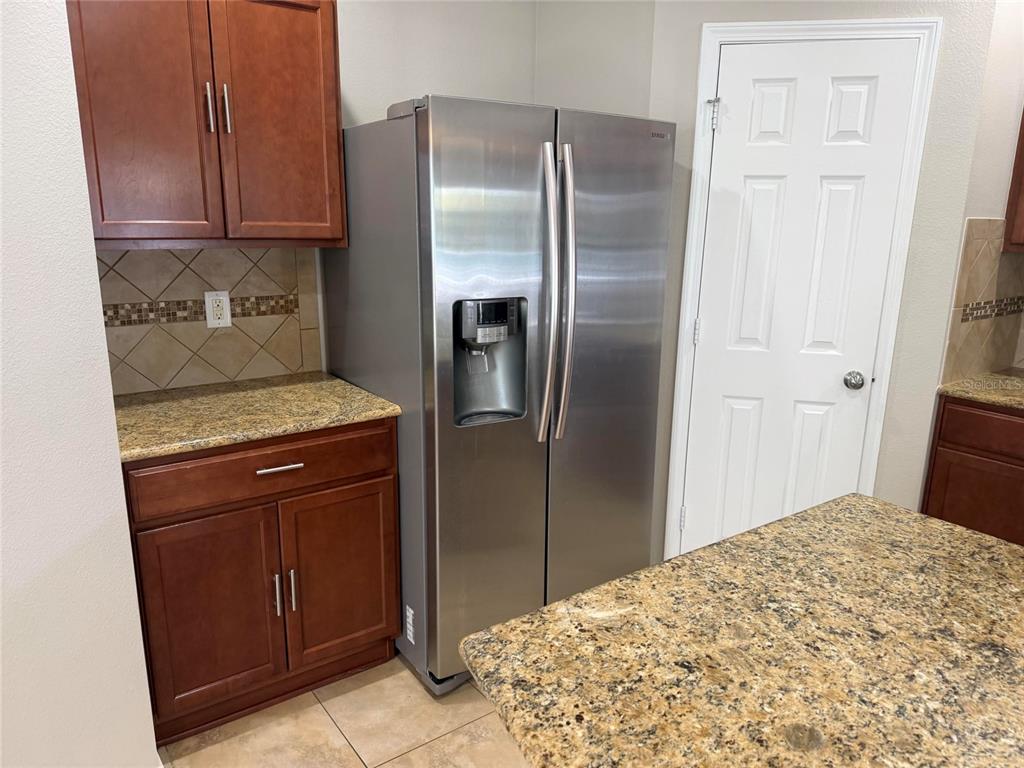 A kitchen features dark wood cabinets, granite countertops, a stainless steel refrigerator, and tile flooring — 4723 SOMERSET HILL LANE, RIVERVIEW, FL