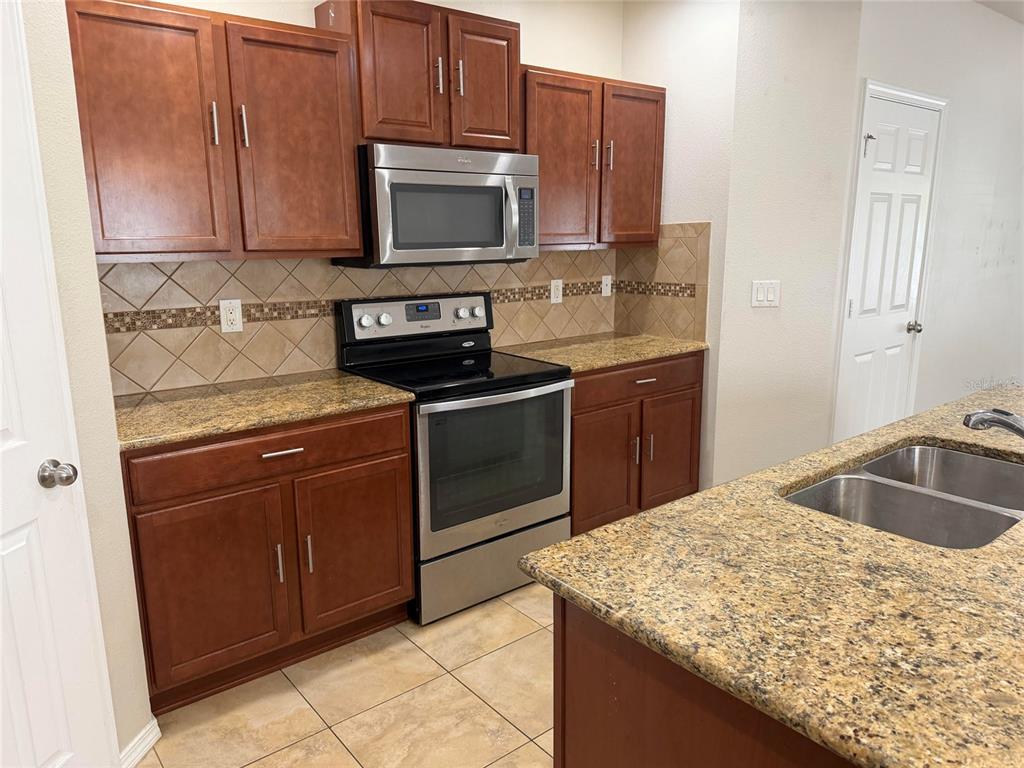 A kitchen features wood cabinets, granite countertops, stainless steel appliances, and a tiled backsplash — 4723 SOMERSET HILL LANE, RIVERVIEW, FL