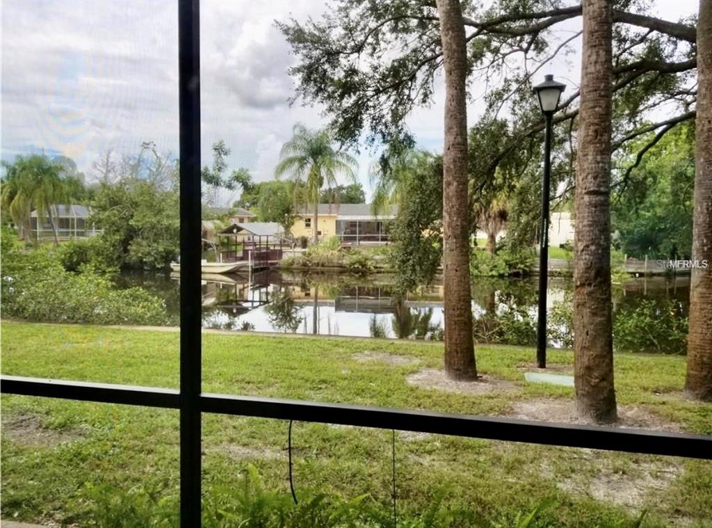 A view of a canal and neighboring houses from behind a screened-in porch — 9119 TUDOR DRIVE UNIT E105, TAMPA, FL
