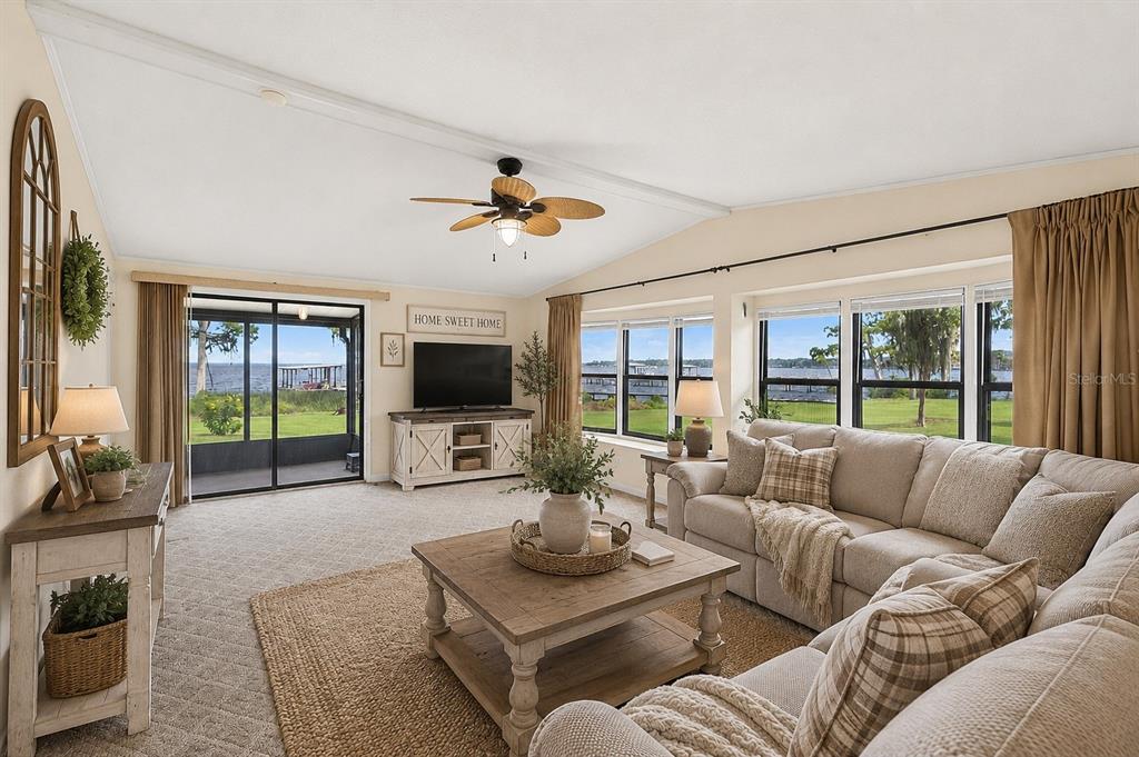 A living room with a vaulted ceiling, beige sofa, and large windows overlooking a lake — 311 POMONA LANDING ROAD, CRESCENT CITY, FL