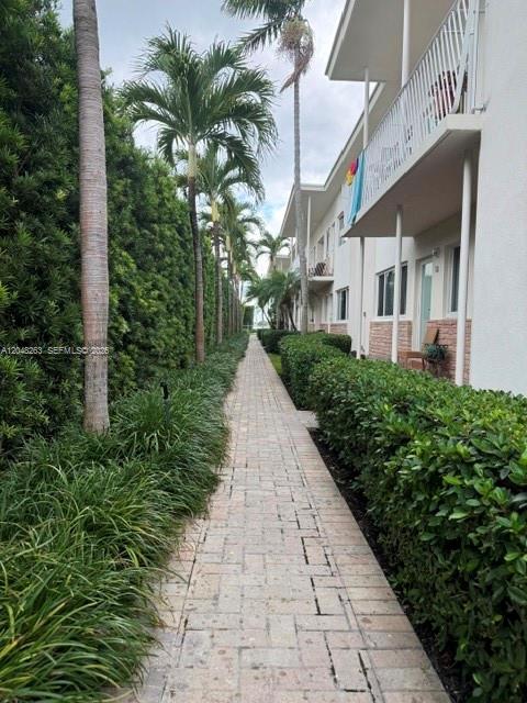 A paved walkway runs between a tall hedge and a multi-story apartment building — 1140 Venetian Way # 2C, Miami FL 33139, MIAMI, FL