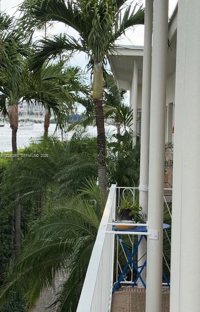 A balcony with a small blue table overlooks palm trees and a body of water — 1140 Venetian Way # 2C, Miami FL 33139, MIAMI, FL