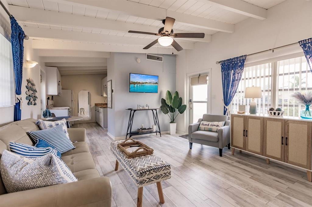 A living room with a ceiling fan, light wood floors, and a television on the wall — 6006 MIDNIGHT PASS ROAD UNIT 10, SARASOTA, FL