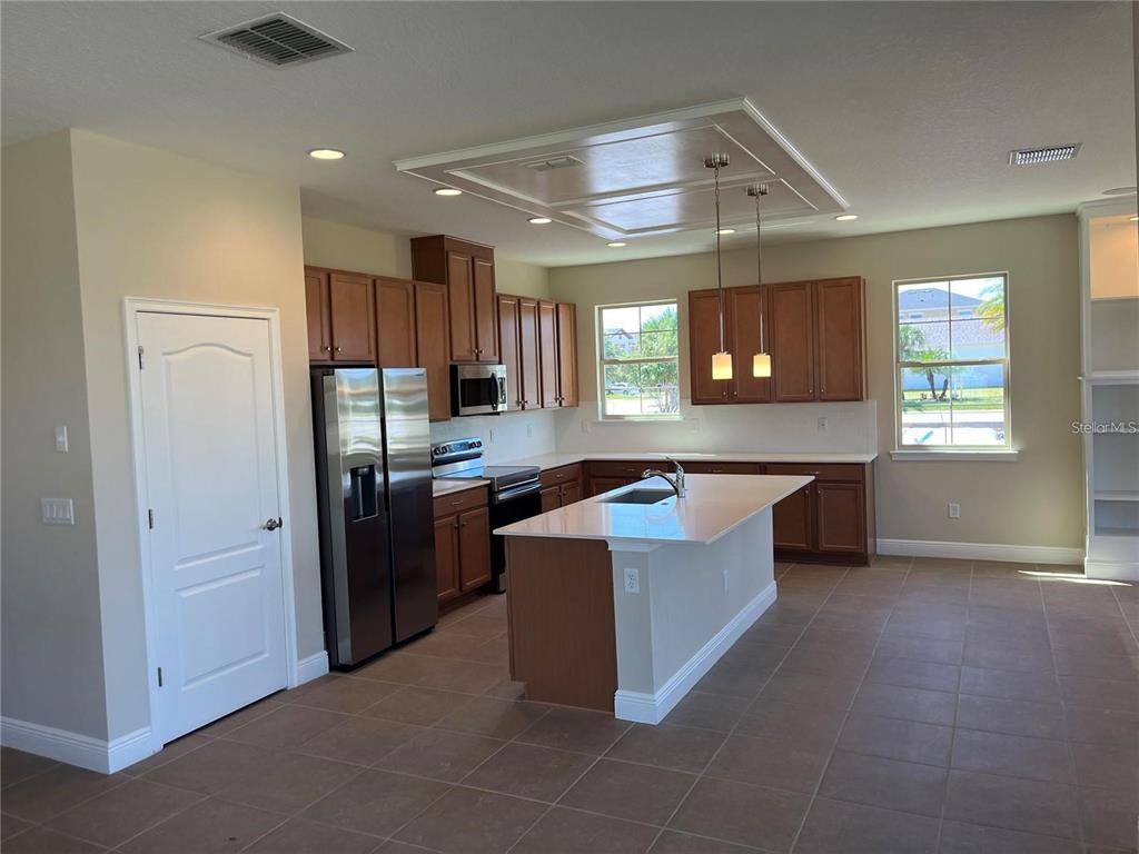 A kitchen features wood cabinets, stainless steel appliances, a center island, and tile flooring — 6673 KNOLLWOOD STREET, HARMONY, FL