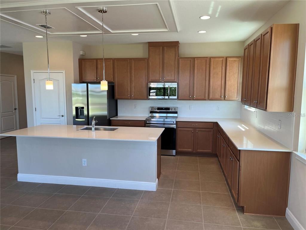 A kitchen features brown wooden cabinets, stainless steel appliances, and a large white island — 6673 KNOLLWOOD STREET, HARMONY, FL
