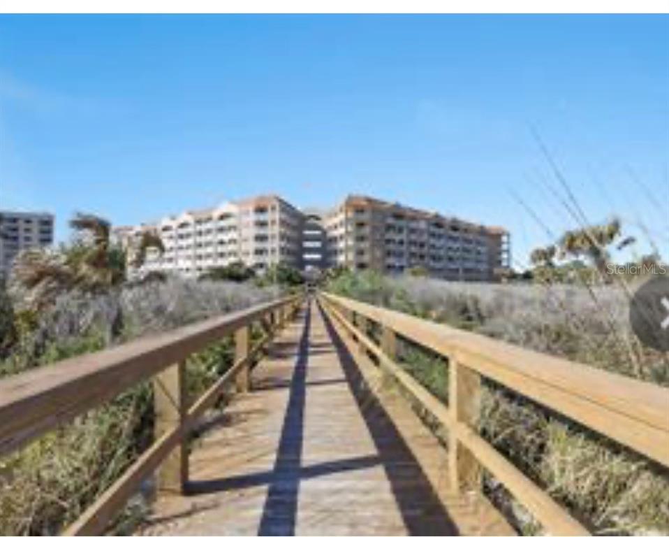 A wooden boardwalk leads through coastal vegetation toward a large multi-story beachfront condominium building — 104 A SURFVIEW DRIVE UNIT 2503, PALM COAST, FL