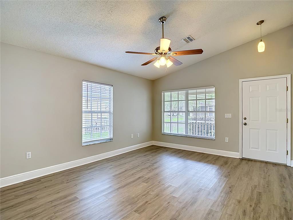 An empty room with light gray walls, wood-look flooring, a ceiling fan, and two windows — 7834 CHADWICK DRIVE, NEW PORT RICHEY, FL