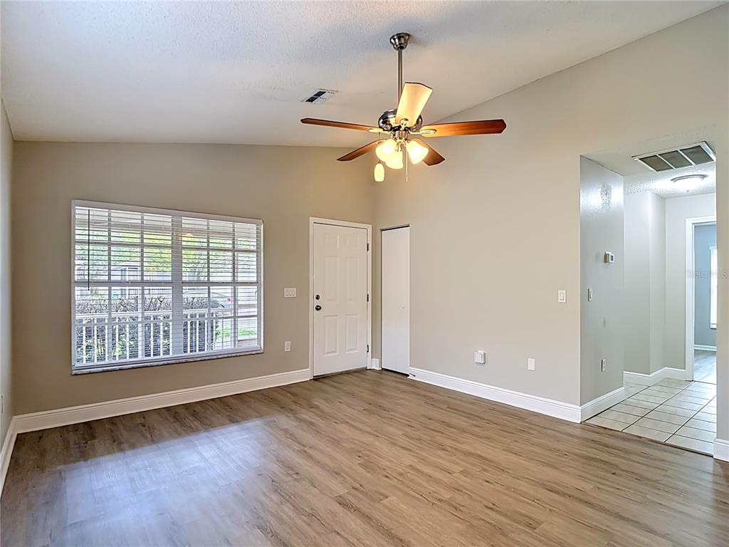 A living room with light-colored walls, wood-look flooring, a ceiling fan, and a window — 7834 CHADWICK DRIVE, NEW PORT RICHEY, FL