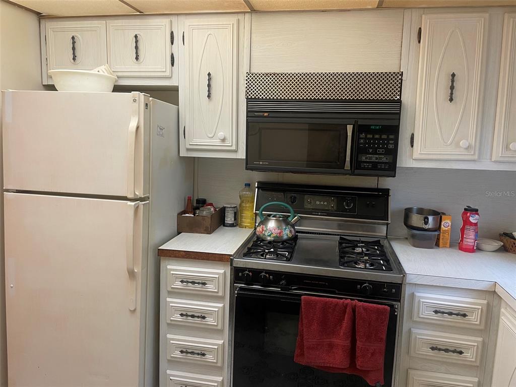 A kitchen features white cabinets, a white refrigerator, and a black stove with a microwave — 5287 81ST STREET N UNIT 12, ST PETERSBURG, FL