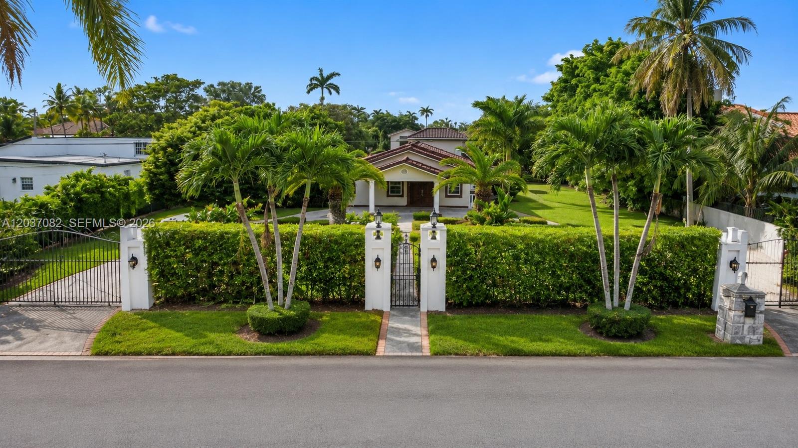 A gated, single-story house with a tiled roof sits behind a manicured hedge and lawn — 300 SW 123rd Ave, Miami FL 33184, MIAMI, FL